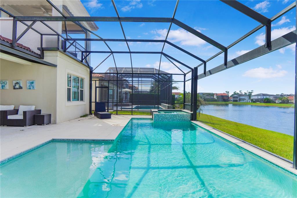 A screened-in pool and spa overlook a lake behind a two-story house — 10751 ROYAL CYPRESS WAY, ORLANDO, FL