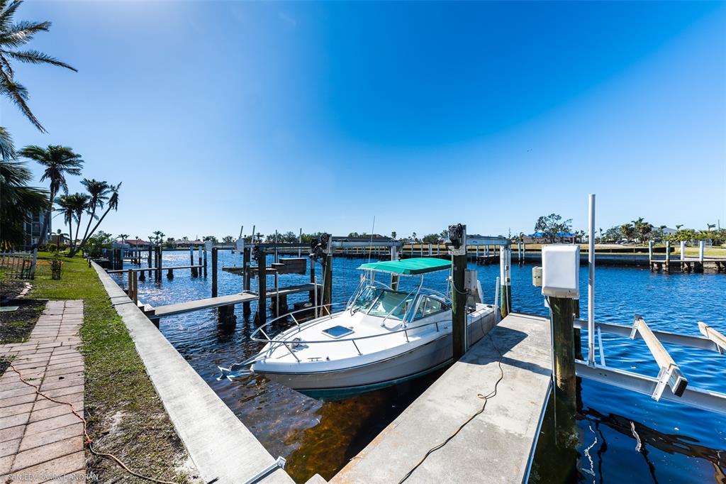 A white motorboat is docked at a concrete pier along a canal under a blue sky — 290 LEWIS CIRCLE UNIT 131, PUNTA GORDA, FL