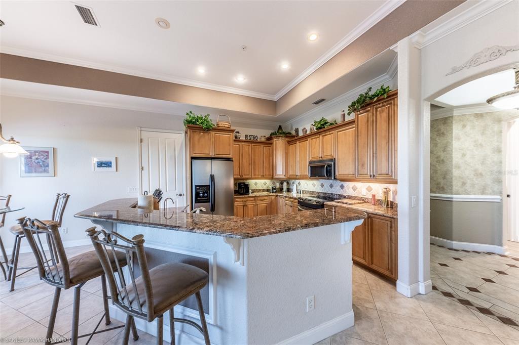 A kitchen features wood cabinets, granite countertops, a breakfast bar with stools, and tile flooring — 290 LEWIS CIRCLE UNIT 131, PUNTA GORDA, FL