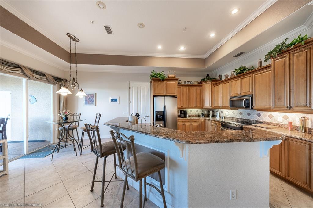 A kitchen with wood cabinets, granite countertops, and a breakfast bar with stools — 290 LEWIS CIRCLE UNIT 131, PUNTA GORDA, FL
