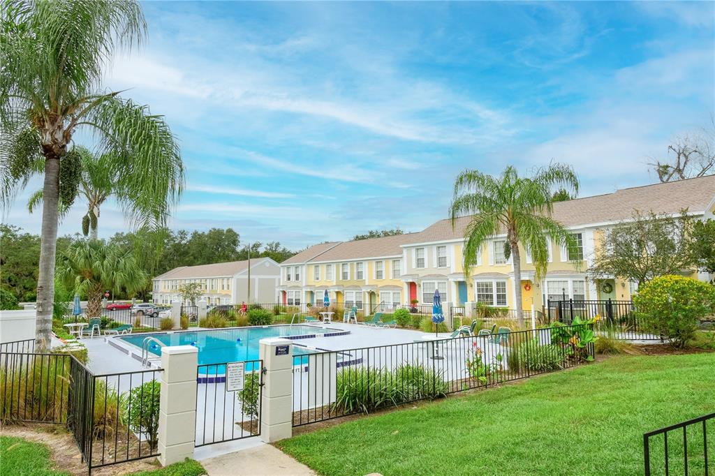 A swimming pool sits in front of a row of multi-story townhomes with palm trees — 13538 EMBASSY PARK COURT UNIT 44A2, DADE CITY, FL