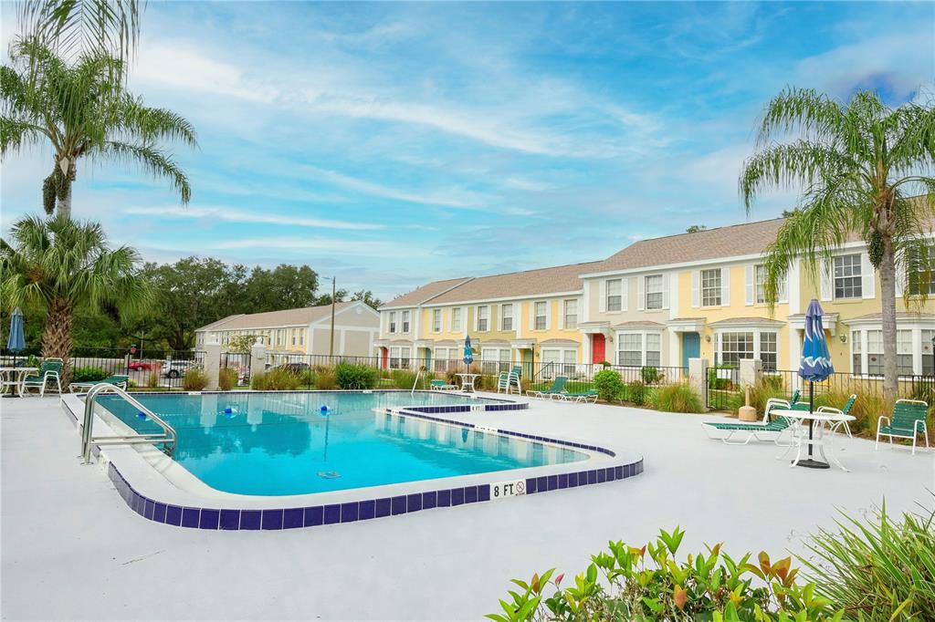 A swimming pool sits in front of a row of multi-story townhomes with palm trees — 13538 EMBASSY PARK COURT UNIT 44A2, DADE CITY, FL