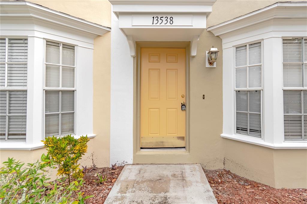 A yellow front door is centered between two bay windows on a tan exterior wall — 13538 EMBASSY PARK COURT UNIT 44A2, DADE CITY, FL