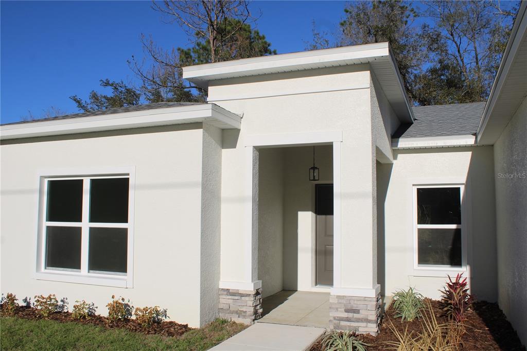 A modern single-story house exterior with white stucco walls, stone accents, and a covered entryway — 9719 N SANDREE DRIVE, CITRUS SPRINGS, FL