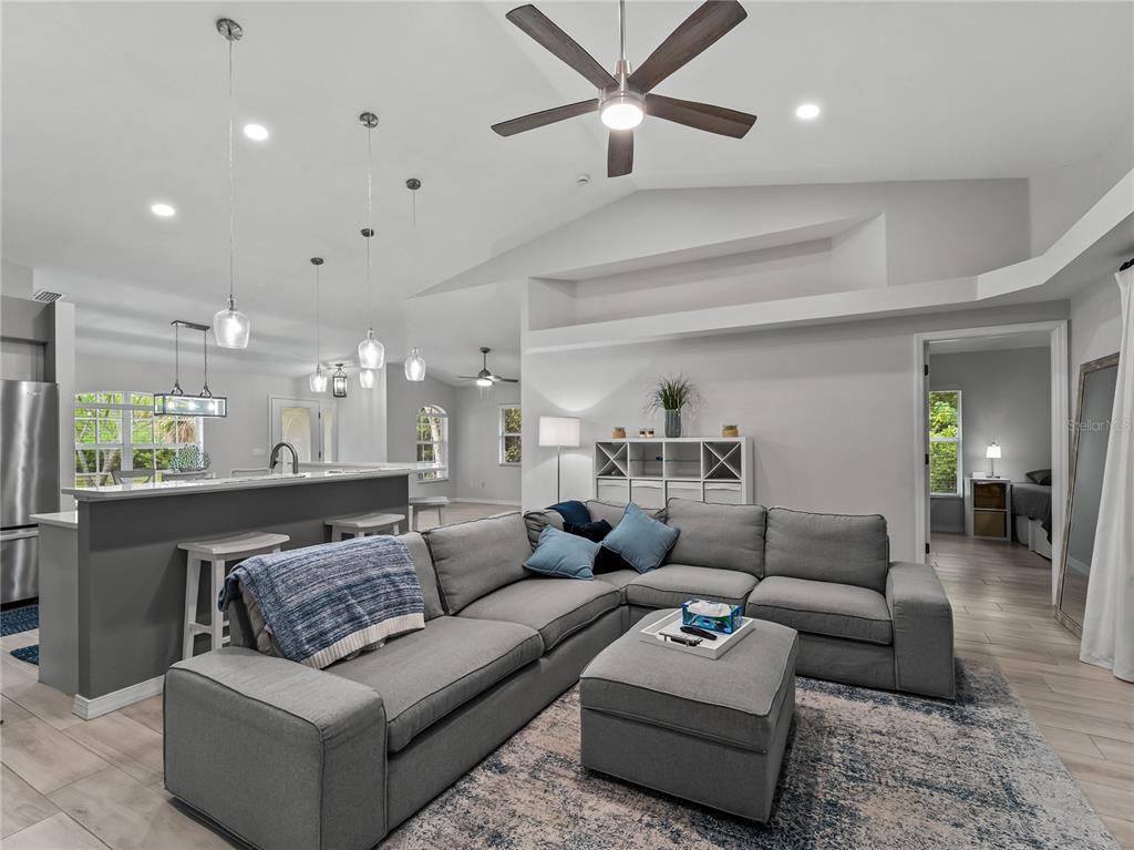 A living room with a gray sectional sofa and ottoman opens to a kitchen area — 145 CREVALLE ROAD, ROTONDA WEST, FL