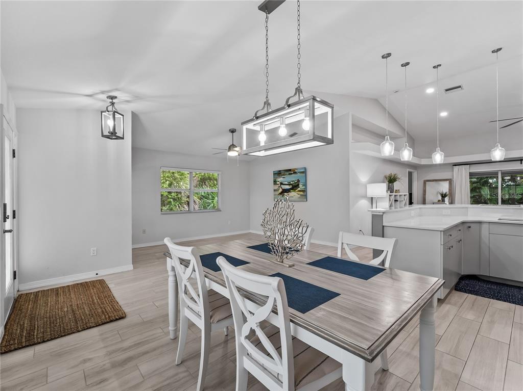 A dining area with a light wood table, white chairs, and a rectangular pendant light — 145 CREVALLE ROAD, ROTONDA WEST, FL