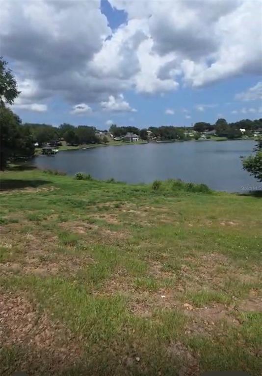 A grassy yard slopes down toward a lake under a cloudy blue sky — S LAKESHORE, EUSTIS, FL