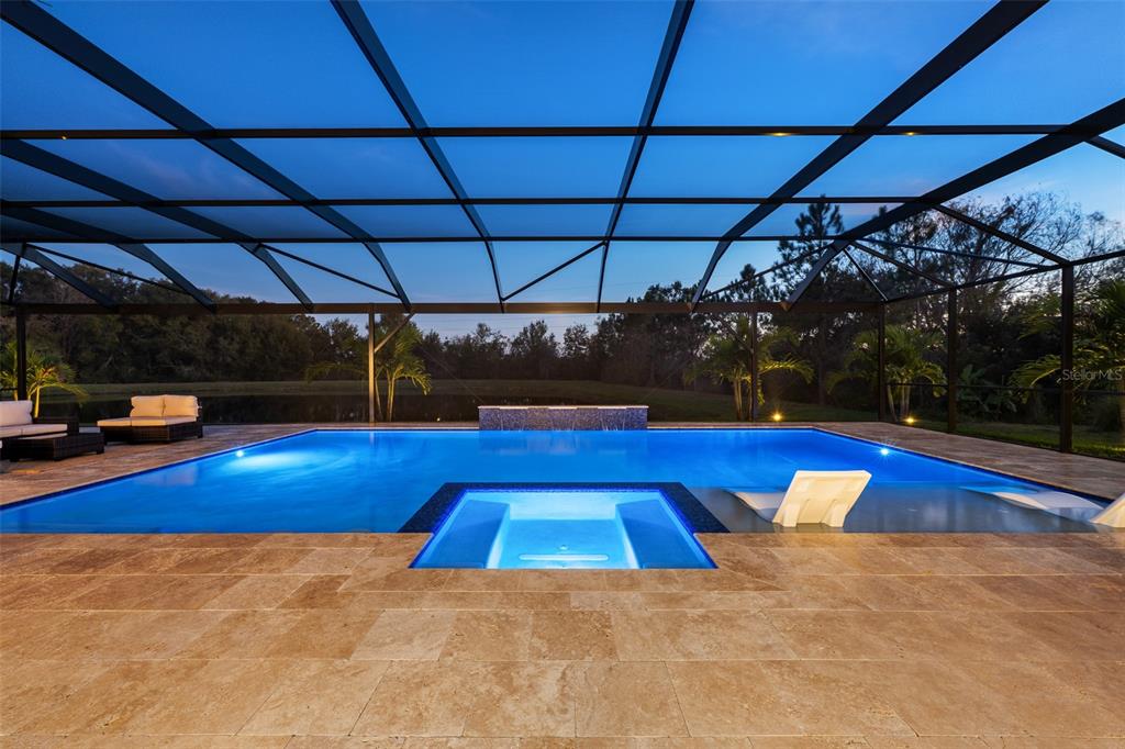 A rectangular swimming pool with an integrated spa sits inside a screened-in patio enclosure — 33376 KATELAND DRIVE, WESLEY CHAPEL, FL