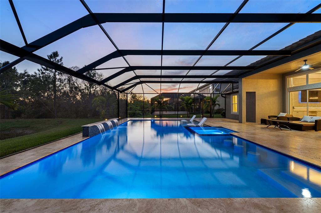 A screened-in swimming pool with a spa and water features sits on a stone patio — 33376 KATELAND DRIVE, WESLEY CHAPEL, FL