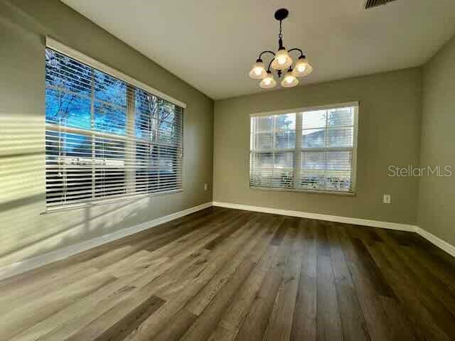 An empty room features light wood-look flooring, two windows with blinds, and a hanging chandelier — 6335 MAISIE ROAD, ZEPHYRHILLS, FL