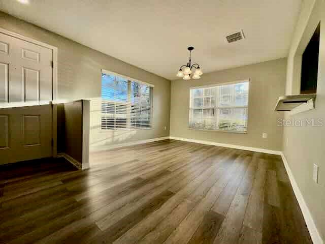 An empty room features light gray walls, wood-look flooring, two windows, and a chandelier — 6335 MAISIE ROAD, ZEPHYRHILLS, FL