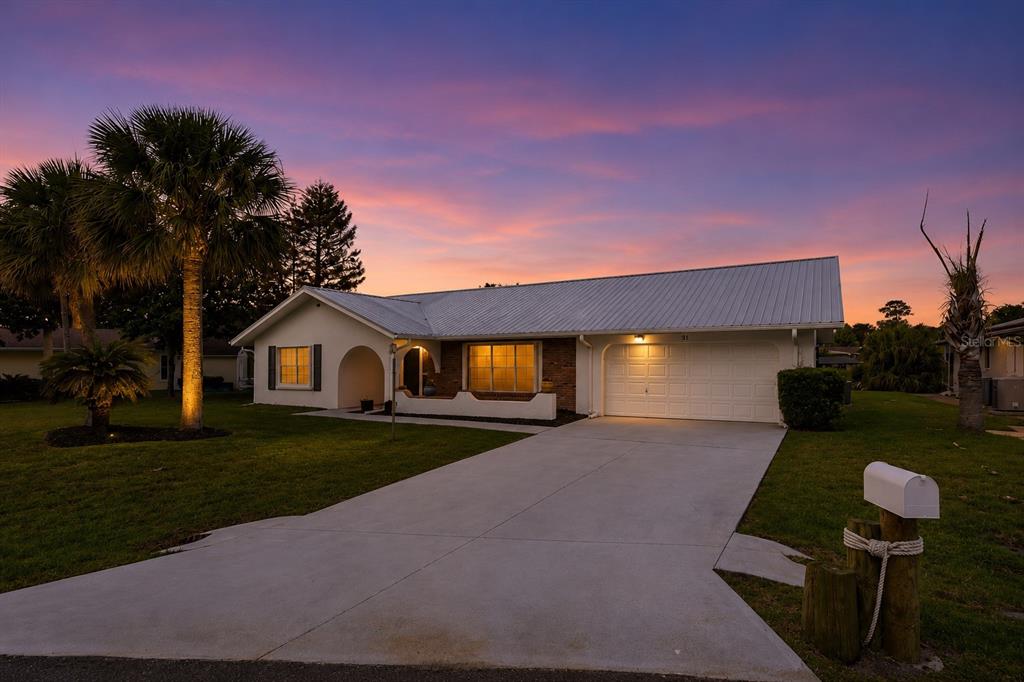 A single-story house with a white metal roof and a concrete driveway at sunset — 31 FLEMING COURT, PALM COAST, FL