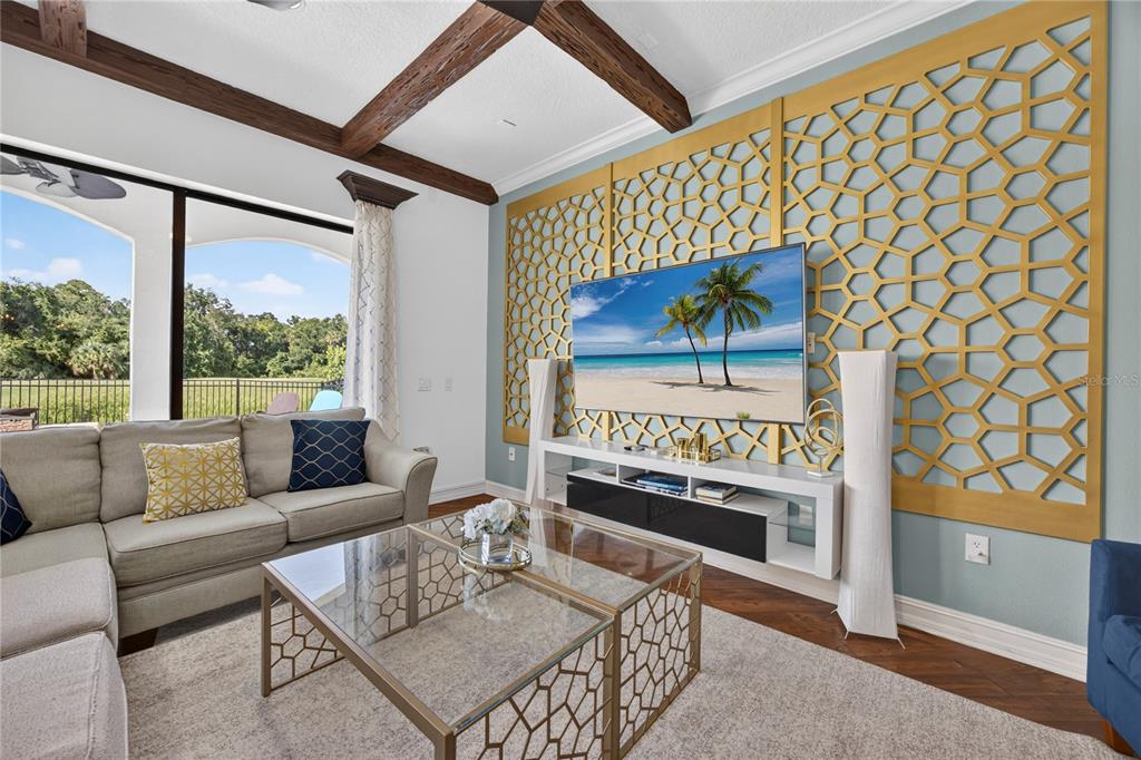 A living room features a gold geometric wall panel, wood ceiling beams, and a glass-topped table — 865 DESERT MOUNTAIN COURT, REUNION, FL