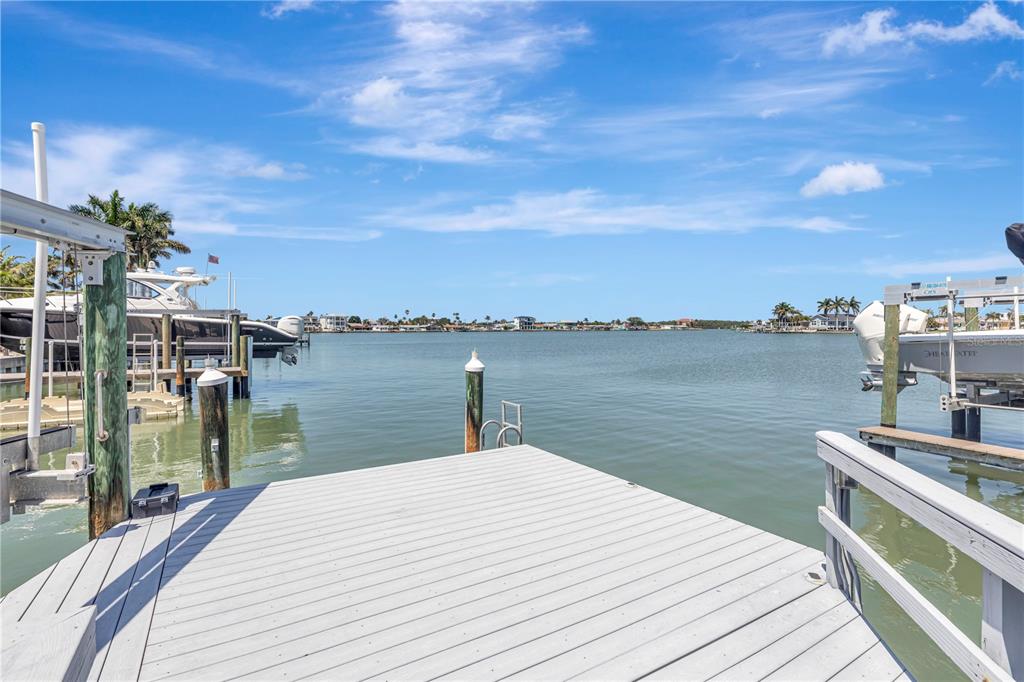 A wooden boat dock extends over calm water with boat lifts on either side — 308 173RD AVENUE E, NORTH REDINGTON BEACH, FL