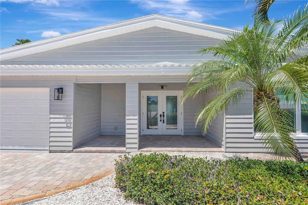 The exterior of a gray house features a paved driveway, double front doors, and landscaping — 308 173RD AVENUE E, NORTH REDINGTON BEACH, FL