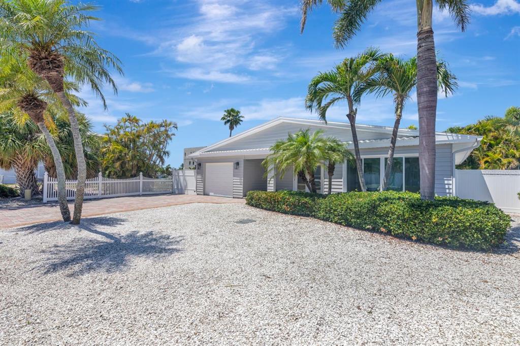 A single-story house with a gravel driveway, palm trees, and a white picket fence — 308 173RD AVENUE E, NORTH REDINGTON BEACH, FL