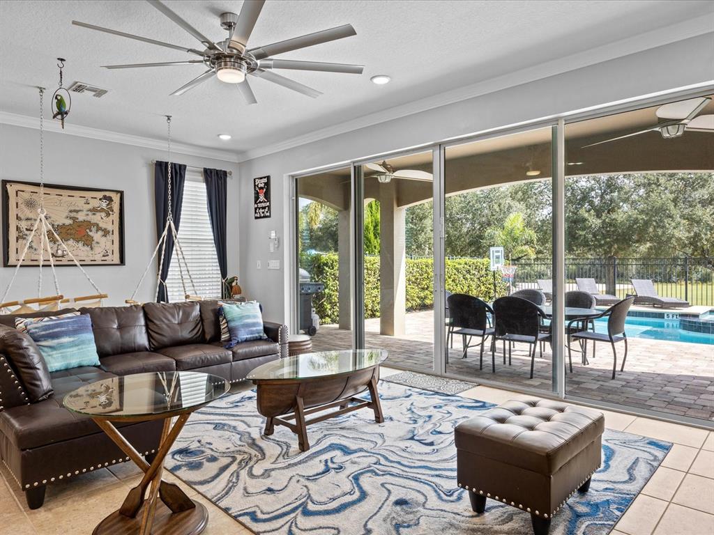 A living room with a leather sofa, glass coffee tables, and sliding doors to a pool — 761 DESERT MOUNTAIN COURT, KISSIMMEE, FL