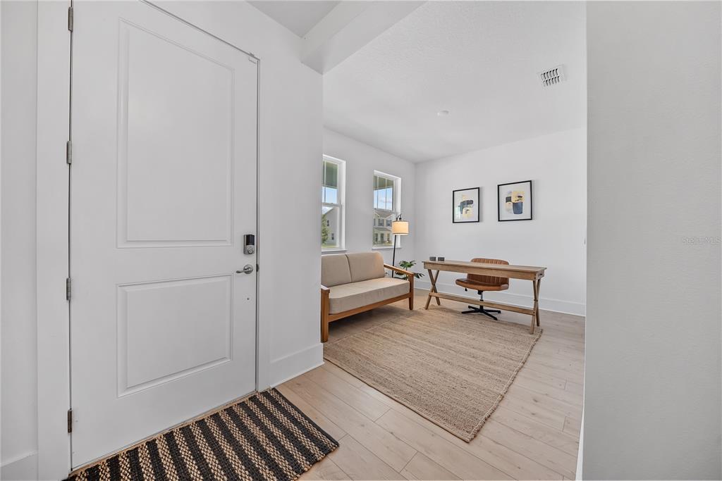 A bright home office features light wood flooring, a beige sofa, and a wooden desk — 1694 PINECLIFF DRIVE, APOPKA, FL