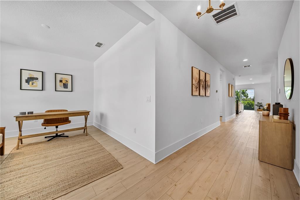 A bright home office area with a wooden desk sits beside a hallway leading outdoors — 1694 PINECLIFF DRIVE, APOPKA, FL