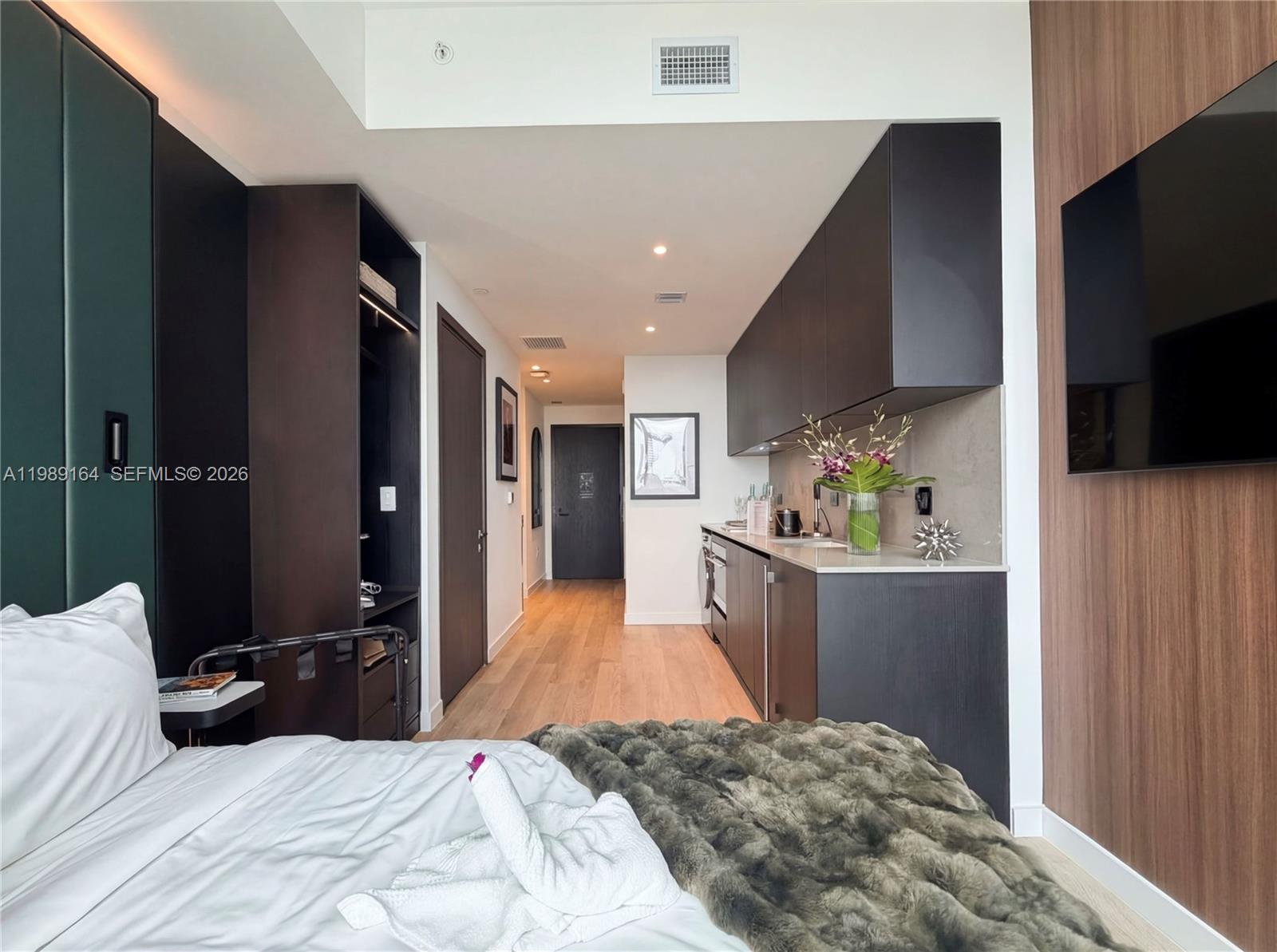 A studio apartment features a kitchenette with dark cabinetry, wood flooring, and a bed — 20 NE 11th St # 4803A, Miami FL 33132, MIAMI, FL