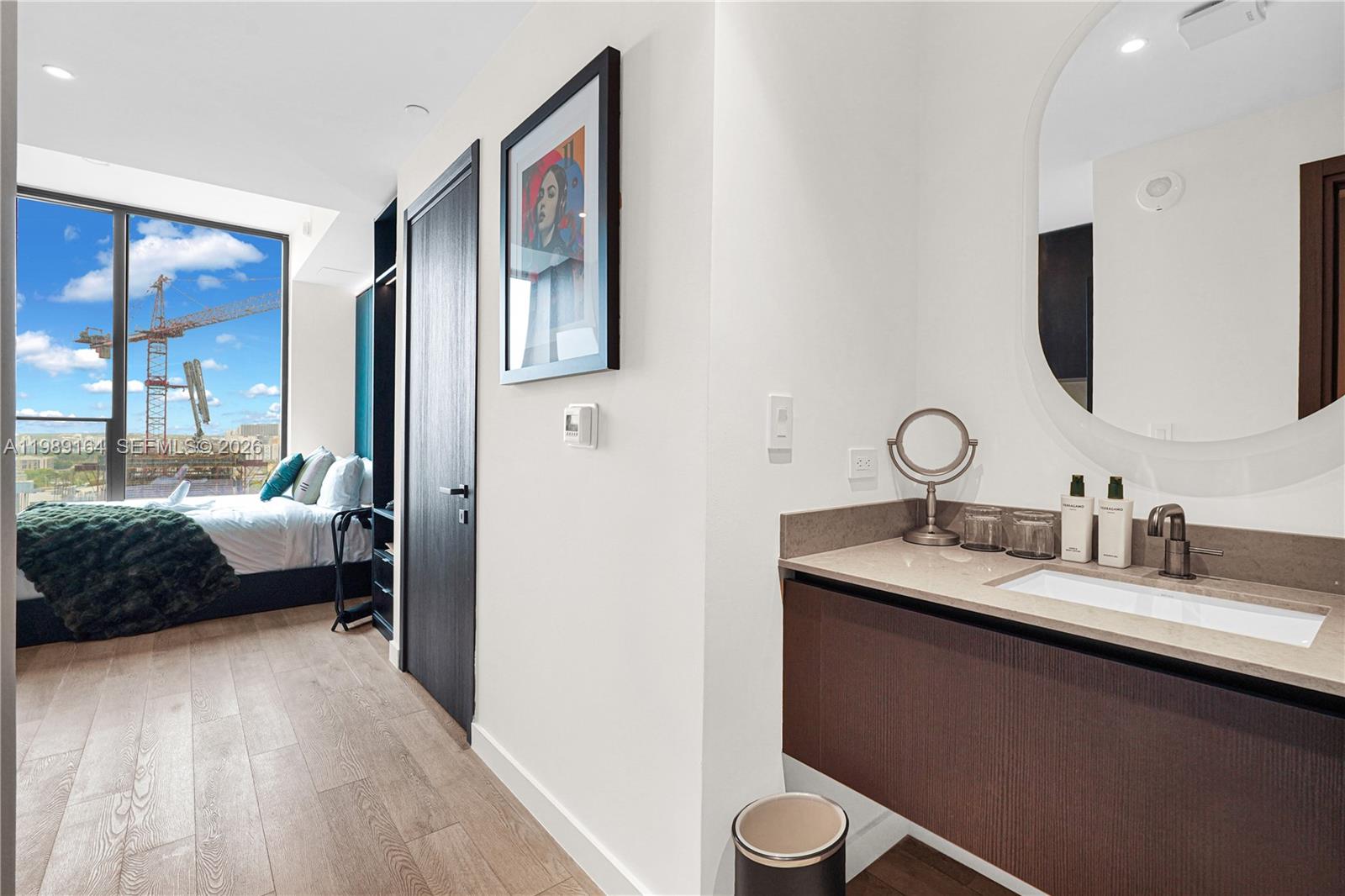 A modern bedroom features a vanity area, wood flooring, and a view of a construction crane — 20 NE 11th St # 4803A, Miami FL 33132, MIAMI, FL