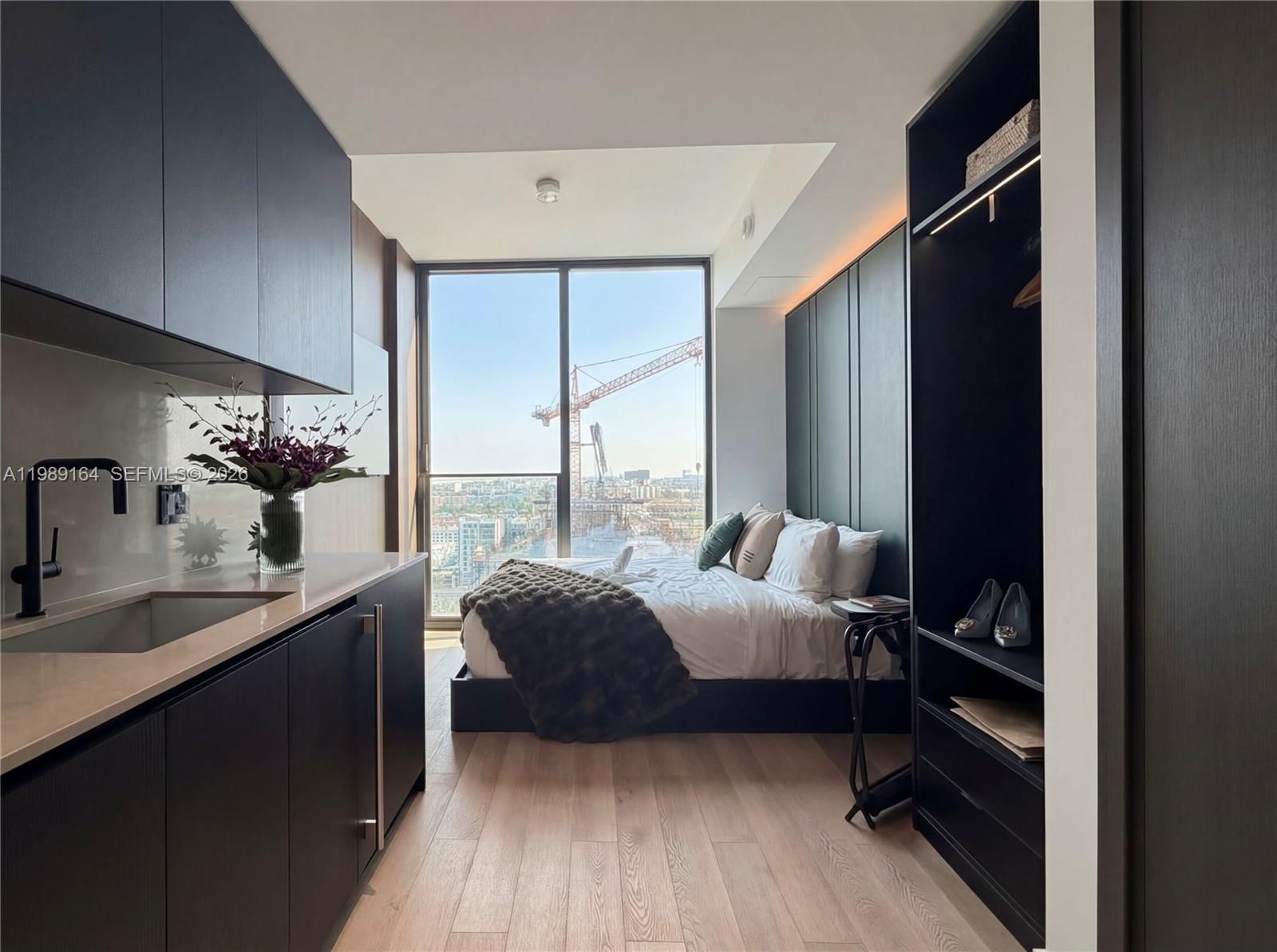A studio apartment features a kitchenette, a bed, and floor-to-ceiling windows overlooking a construction site — 20 NE 11th St # 4803A, Miami FL 33132, MIAMI, FL
