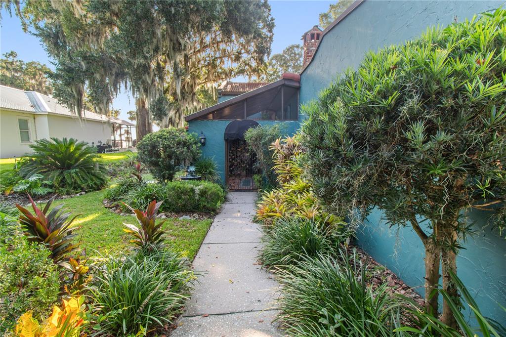 A concrete walkway leads to a teal-colored house entrance surrounded by lush landscaping and trees — 1019 W LAKE ELOISE TERRACE, WINTER HAVEN, FL
