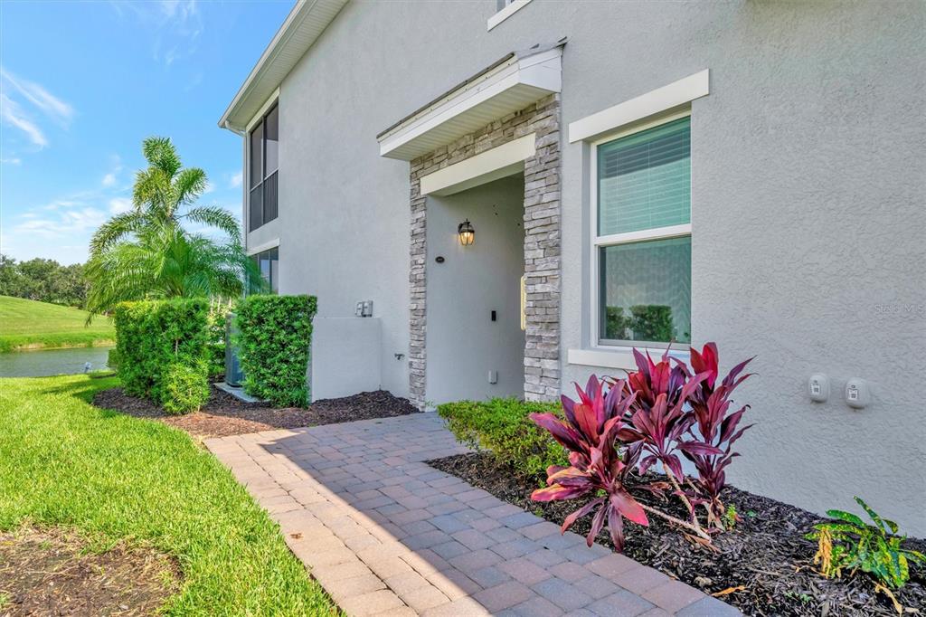 A paved walkway leads to the stone-accented entrance of a gray stucco residential building — 947 TIDEWATER SHORES LOOP, BRADENTON, FL