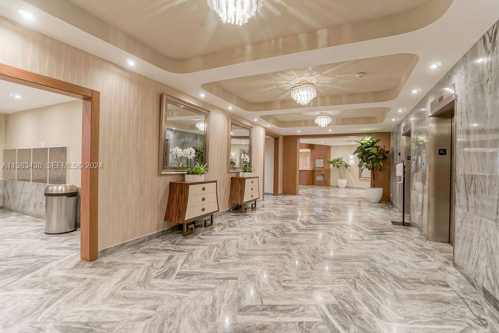 A modern building lobby features marble floors, recessed lighting, crystal chandeliers, and wood-paneled walls — 5401 Collins Ave # 601, Miami Beach FL 33140, MIAMI BEACH, FL