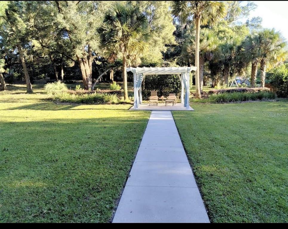 A concrete walkway leads through a grassy lawn to a white pergola with patio furniture — 215 E FRENCH AVENUE, ORANGE CITY, FL
