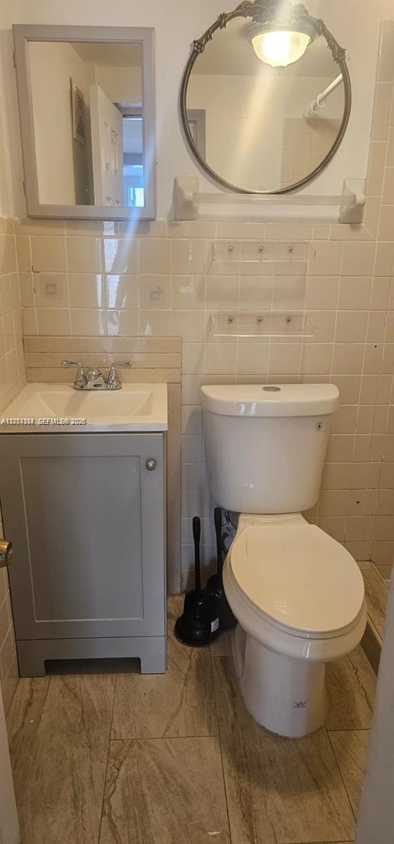 A small bathroom features a gray vanity, a white toilet, and a round wall mirror — 6951 SW 26th St # w, Miramar FL 33023, MIRAMAR, FL