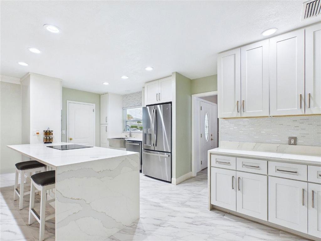 A modern kitchen features white cabinets, a marble-topped island with seating, and stainless steel appliances — 409 4TH AVENUE N, TIERRA VERDE, FL
