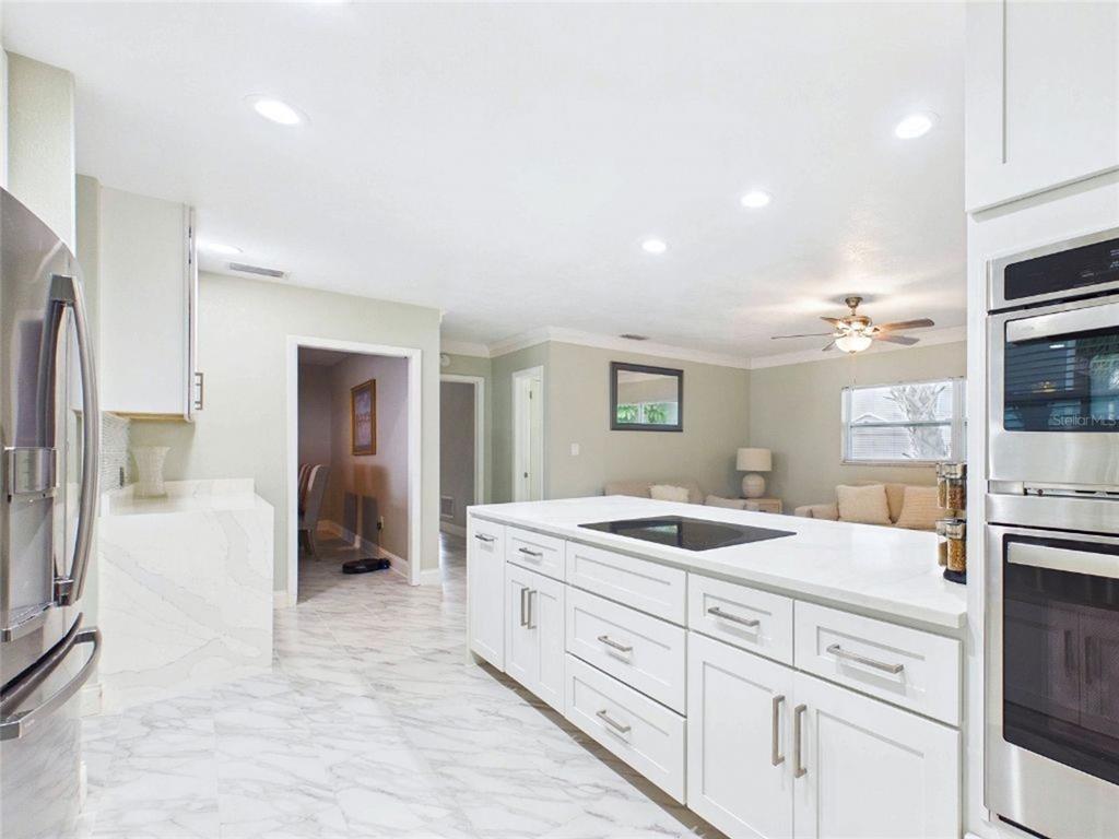 A modern kitchen with white cabinets, marble-look floors, and a large island with a cooktop — 409 4TH AVENUE N, TIERRA VERDE, FL