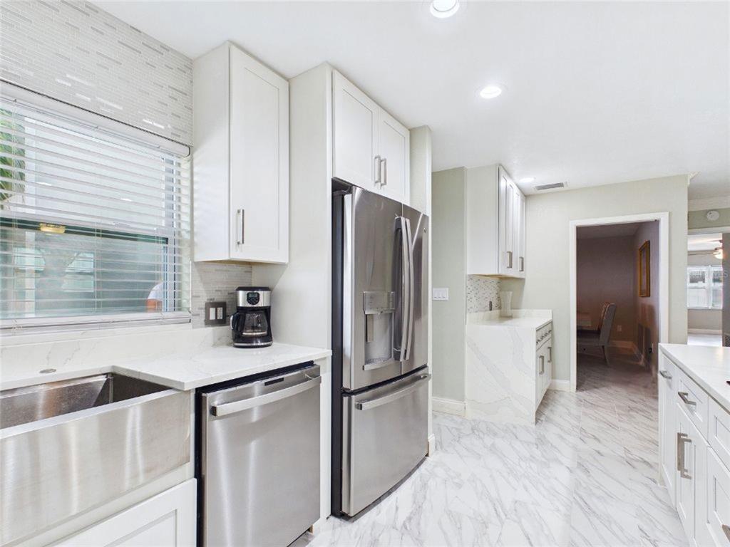 A kitchen with white cabinets, stainless steel appliances, marble-patterned countertops, and light-colored tile flooring — 409 4TH AVENUE N, TIERRA VERDE, FL