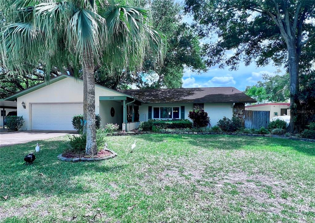 A house with solar panels on its roof sits behind a pond and lush trees — 2219 ALICE LANE, CLEARWATER, FL