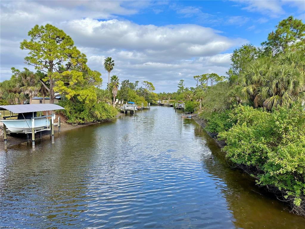 A narrow canal flows between lush green vegetation and private boat docks under a cloudy sky — 1327 CLEARVIEW DRIVE, PORT CHARLOTTE, FL