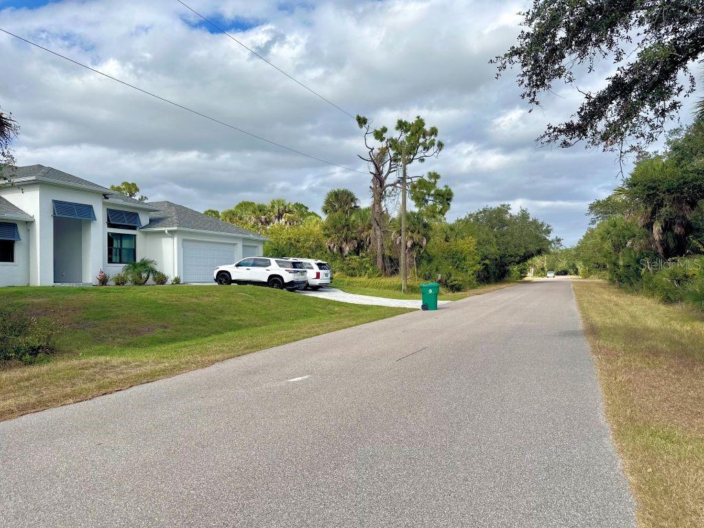 A white house with a two-car garage sits beside a paved road with vegetation — 1327 CLEARVIEW DRIVE, PORT CHARLOTTE, FL