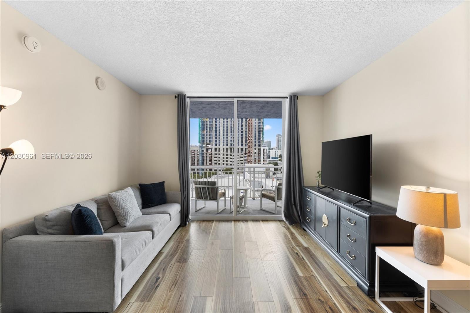 A living room features a gray sofa, a dark media console, and a balcony view — 275 NE 18th St # 710, Miami FL 33132, MIAMI, FL