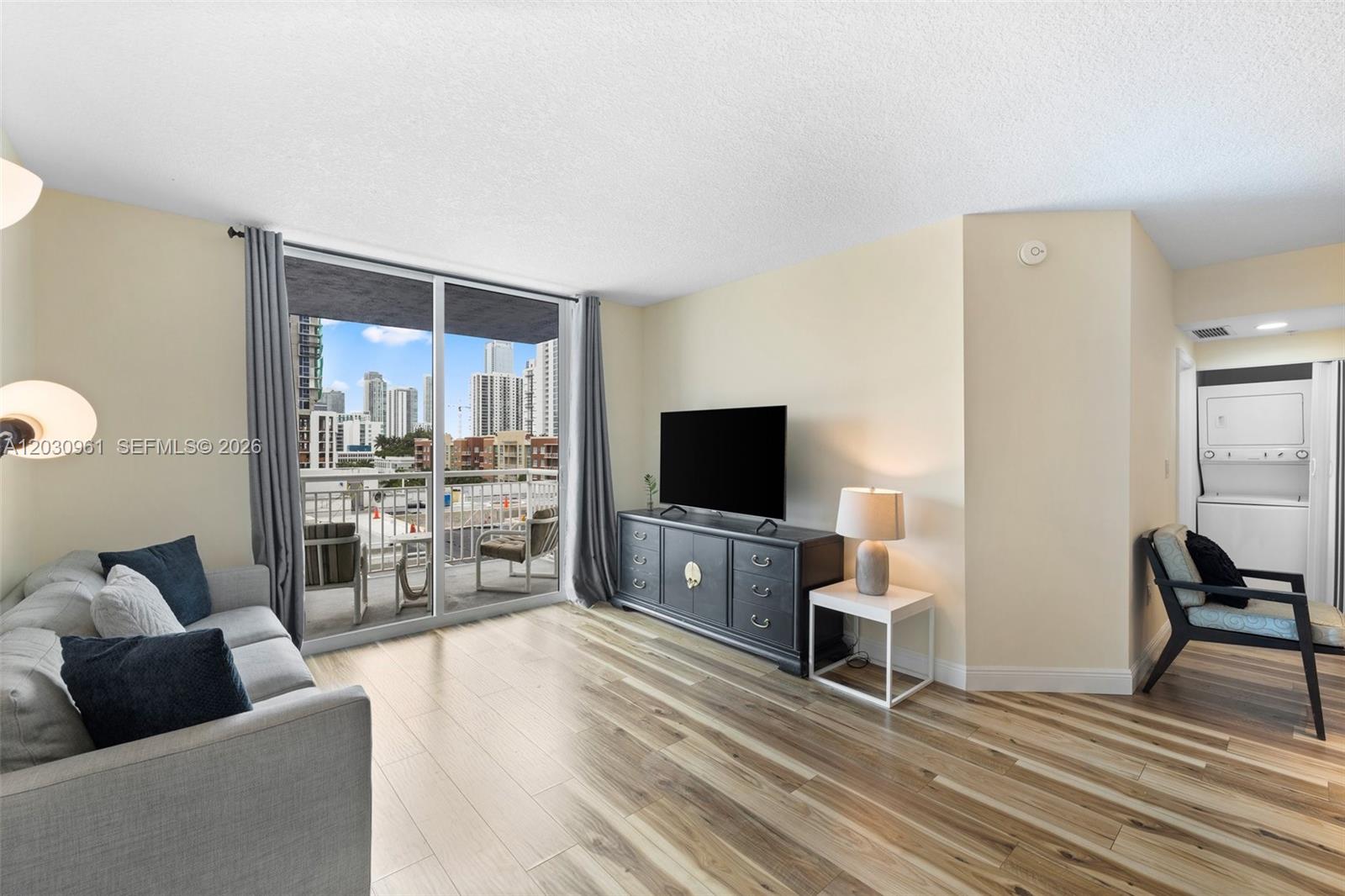 A living room features wood-look flooring, a gray sofa, a media console, and a balcony — 275 NE 18th St # 710, Miami FL 33132, MIAMI, FL