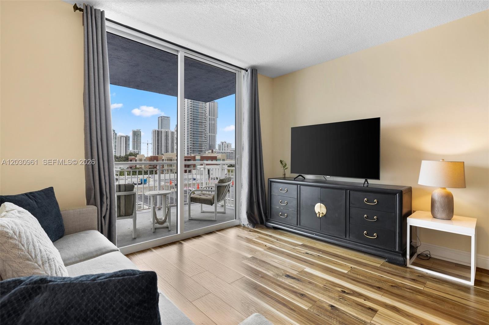 A living room features wood flooring, a television console, and a balcony with city views — 275 NE 18th St # 710, Miami FL 33132, MIAMI, FL