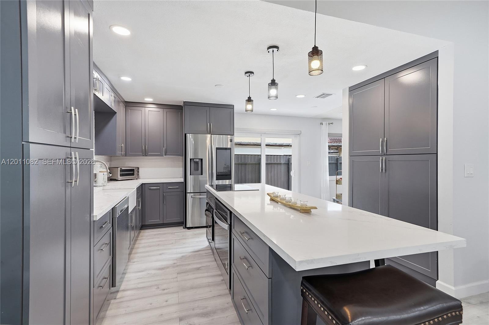 A modern kitchen features gray cabinets, a large white quartz island, and stainless steel appliances — 20102 NW 62nd Ave, Miami FL 33015, MIAMI, FL