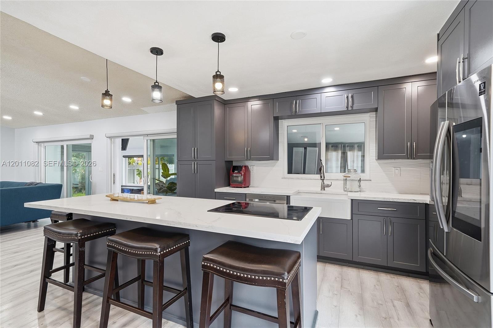 A modern kitchen features dark gray cabinetry, a white quartz island, and three pendant lights — 20102 NW 62nd Ave, Miami FL 33015, MIAMI, FL