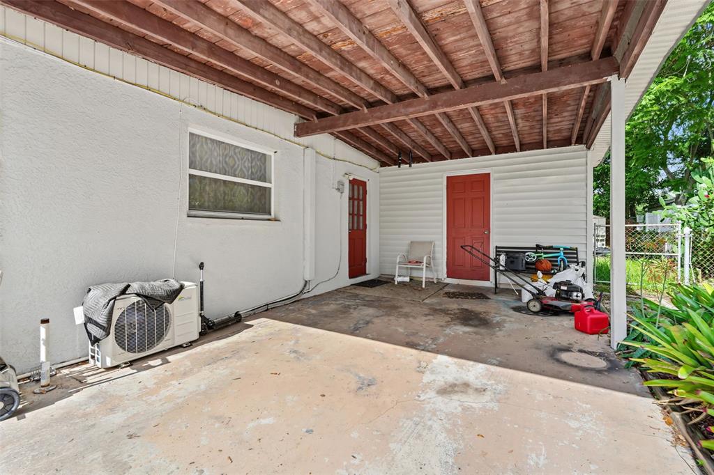 A covered concrete patio features two red doors, a window, and an outdoor HVAC unit — 9374 84TH STREET, SEMINOLE, FL