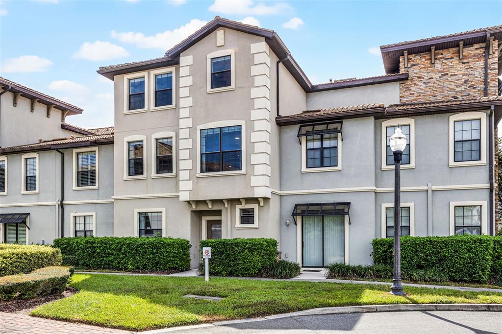 A three-story townhouse with a stucco facade, stone accents, and a manicured hedge — 1317 SHINNECOCK HILLS DRIVE, DAVENPORT, FL