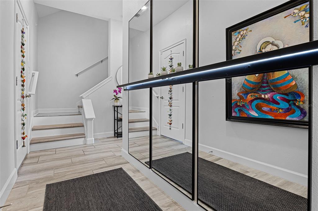 An entryway features light wood-look tile flooring, a staircase, and a large wall of mirrors — 1317 SHINNECOCK HILLS DRIVE, DAVENPORT, FL