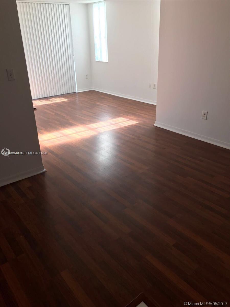 An empty room features dark wood-look flooring, white walls, and a large sliding glass door — 4420 NW 107th Ave # 207, Doral FL 33178, DORAL, FL