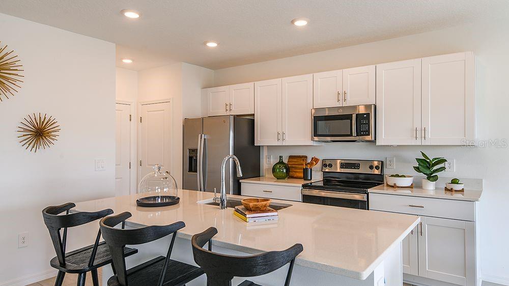 A modern kitchen features white cabinets, stainless steel appliances, and a large quartz-topped island — 140 BRINSMEAD ROAD, HAINES CITY, FL