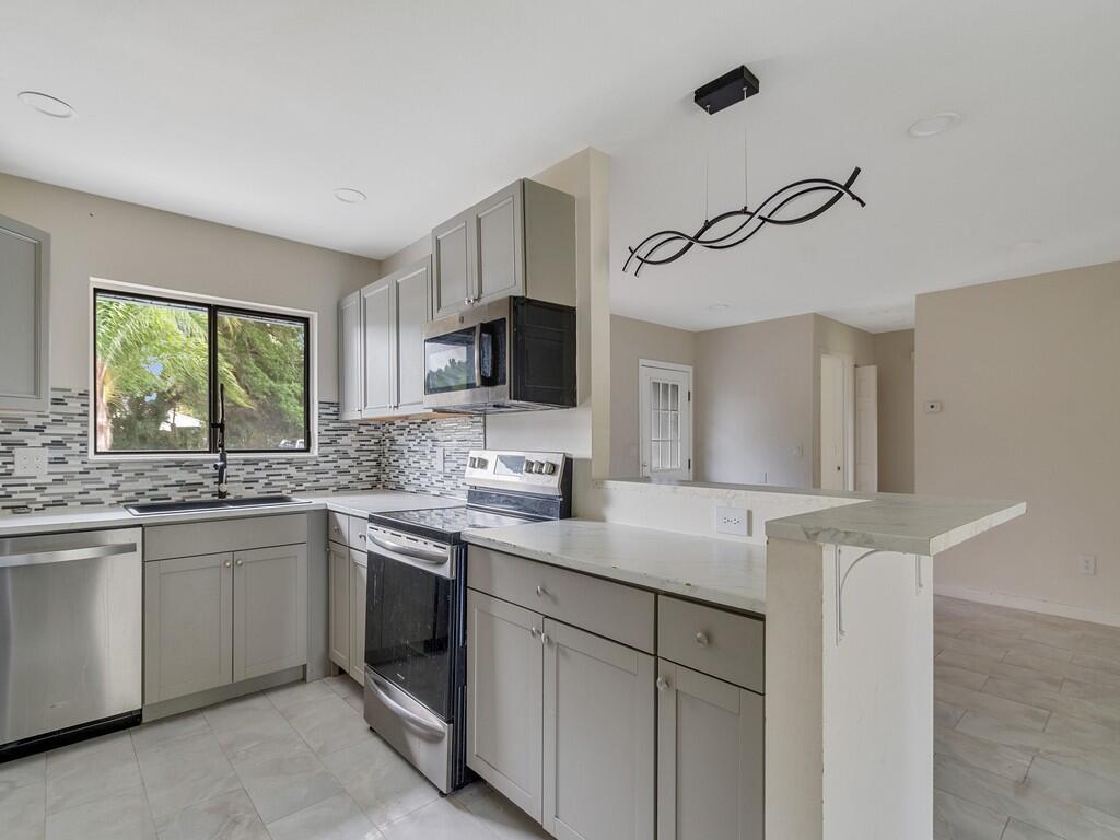 A kitchen with gray cabinets, stainless steel appliances, a tiled backsplash, and a breakfast bar — 1846 24th Place SW, Vero Beach FL 32962, VERO BEACH, FL