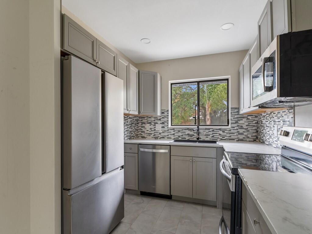 A kitchen with grey cabinets, stainless steel appliances, a tiled backsplash, and a window — 1846 24th Place SW, Vero Beach FL 32962, VERO BEACH, FL