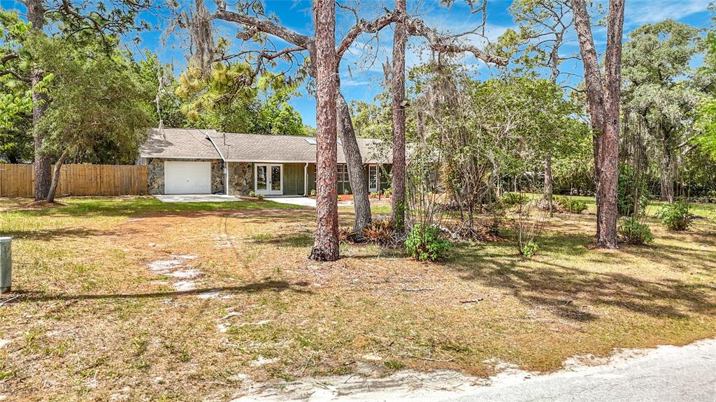 A single-story house with a stone facade and attached garage sits on a wooded lot — 13206 TYRONE STREET, HUDSON, FL